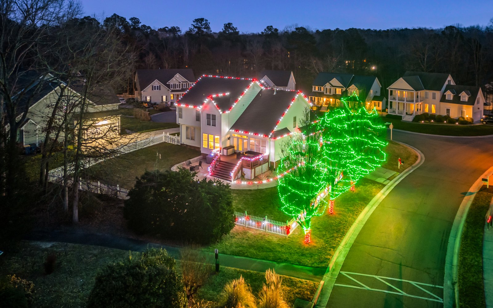 Christmas light installation by Monty's Lighting Co., serving Ashland, VA — a lit porch under a red-and-white roofline, with green-wrapped trees out at the street